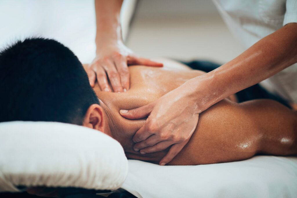 A massage therapist performing a deep tissue back and shoulder massage on a patient lying on a clinic table.
